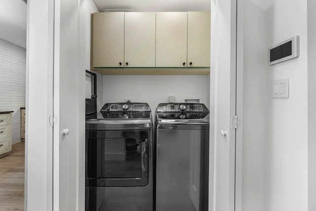 washroom with cabinets, brick wall, separate washer and dryer, and hardwood / wood-style floors