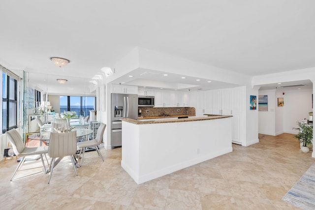 kitchen featuring stainless steel appliances, floor to ceiling windows, white cabinets, stone countertops, and decorative backsplash