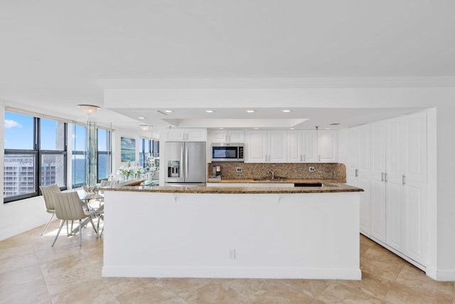 kitchen with white cabinetry, a water view, dark stone counters, stainless steel appliances, and backsplash