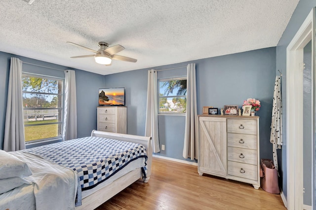 bedroom featuring ceiling fan, multiple windows, light hardwood / wood-style flooring, and a textured ceiling