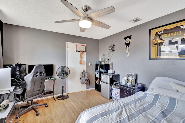 bedroom featuring ceiling fan, a textured ceiling, stainless steel fridge, and light wood-type flooring