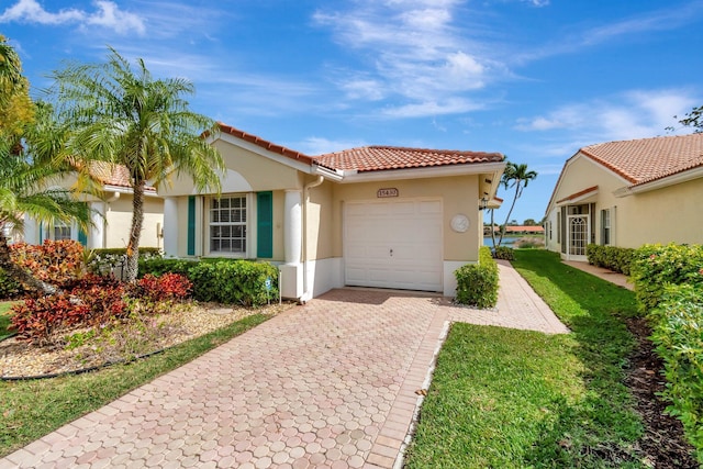 mediterranean / spanish-style house with a tiled roof, an attached garage, decorative driveway, a front yard, and stucco siding