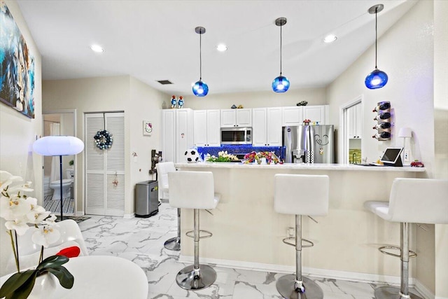 kitchen with pendant lighting, stainless steel appliances, white cabinets, a kitchen bar, and decorative backsplash