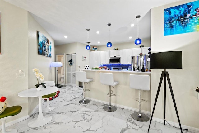 kitchen with pendant lighting, a breakfast bar area, appliances with stainless steel finishes, white cabinetry, and kitchen peninsula