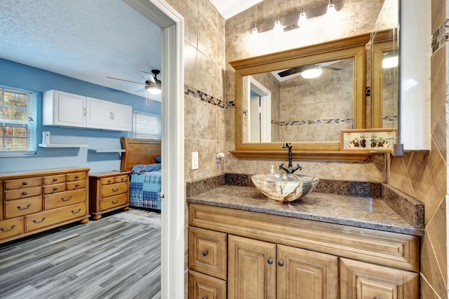 bathroom featuring a textured ceiling, tile walls, vanity, ceiling fan, and hardwood / wood-style floors