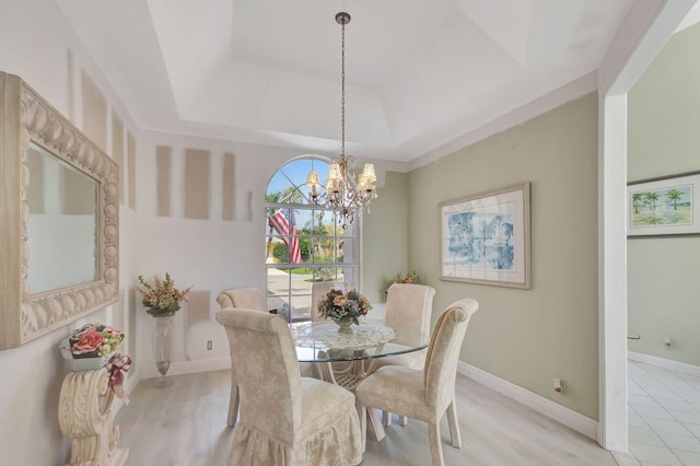 dining area featuring an inviting chandelier, a raised ceiling, and light hardwood / wood-style flooring