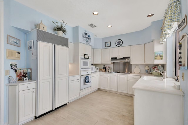 kitchen with built in appliances, sink, light hardwood / wood-style flooring, and white cabinets