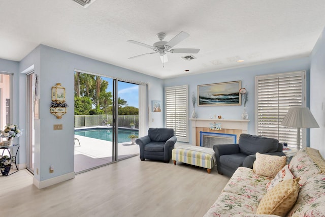 living room featuring ceiling fan, a tiled fireplace, a textured ceiling, and light wood-type flooring