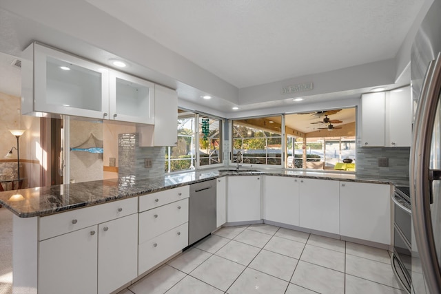 kitchen featuring white cabinetry, stainless steel appliances, tasteful backsplash, kitchen peninsula, and dark stone counters