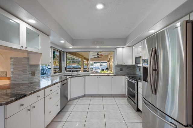 kitchen with appliances with stainless steel finishes, white cabinetry, sink, dark stone countertops, and light tile patterned floors