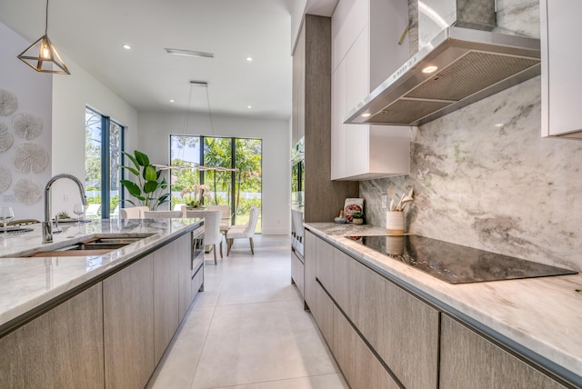 kitchen featuring wall chimney range hood, sink, hanging light fixtures, tasteful backsplash, and black electric stovetop