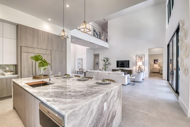 kitchen featuring a towering ceiling, pendant lighting, sink, a large island, and light stone counters