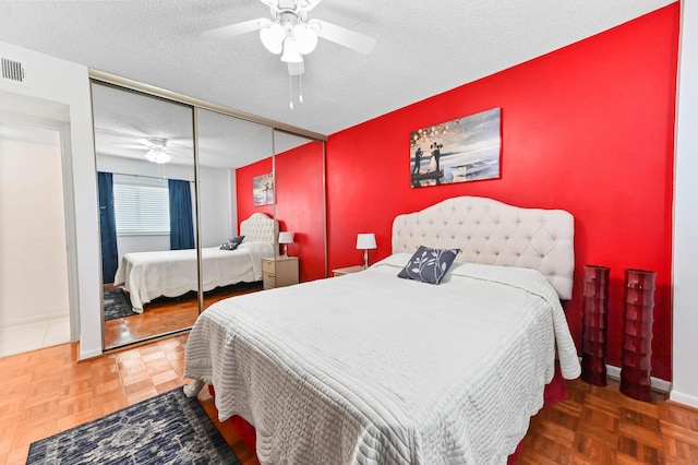 bedroom with a textured ceiling, an accent wall, a ceiling fan, baseboards, and a closet