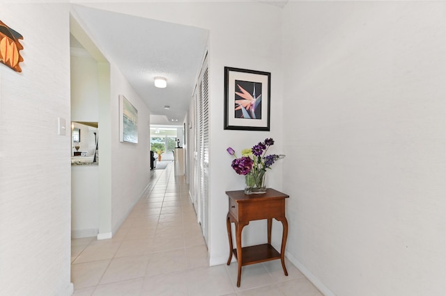 hall featuring light tile patterned flooring and baseboards