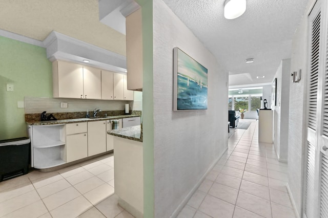 corridor featuring light tile patterned flooring, a sink, a textured ceiling, and baseboards