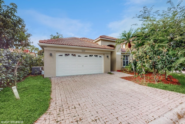 mediterranean / spanish home with central AC unit, a tiled roof, an attached garage, decorative driveway, and stucco siding