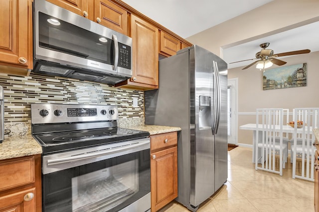 kitchen featuring light stone counters, appliances with stainless steel finishes, light tile patterned flooring, and tasteful backsplash