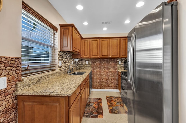 kitchen with sink, light stone counters, light tile patterned floors, stainless steel appliances, and decorative backsplash