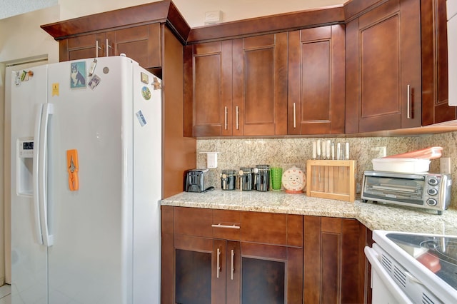 kitchen featuring tasteful backsplash, light stone counters, and white fridge with ice dispenser