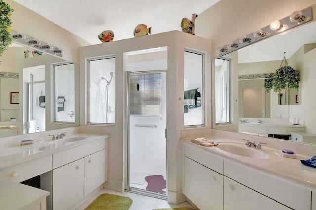 bathroom featuring a wealth of natural light, tile patterned flooring, vanity, walk in shower, and a textured ceiling