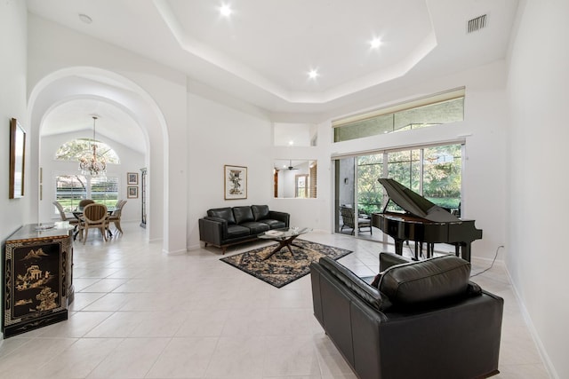 living room featuring a notable chandelier, a tray ceiling, light tile patterned floors, and a high ceiling