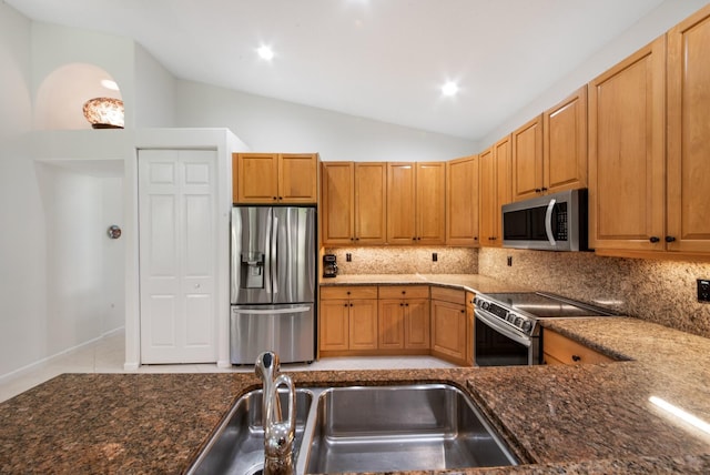 kitchen featuring vaulted ceiling, appliances with stainless steel finishes, sink, dark stone countertops, and backsplash