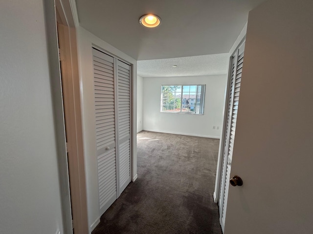 hall featuring dark carpet and a textured ceiling