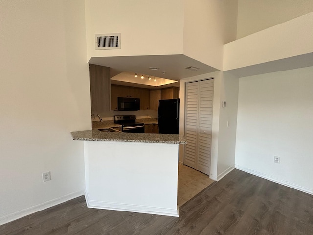 kitchen with sink, black appliances, kitchen peninsula, hardwood / wood-style flooring, and a high ceiling