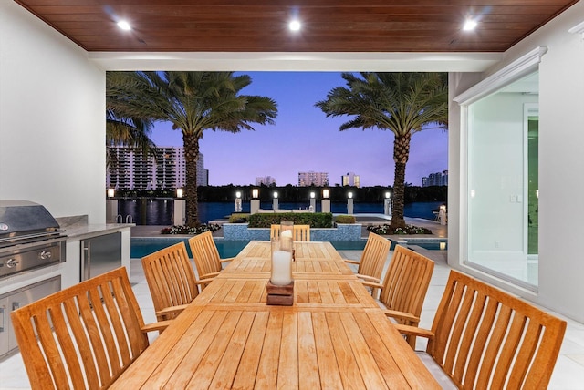 wooden deck with a water view, a view of city, area for grilling, outdoor dining space, and exterior kitchen