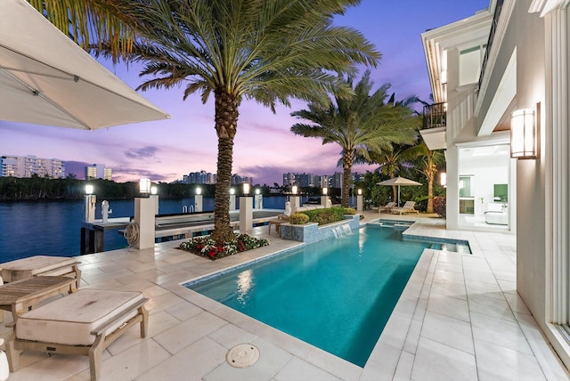 pool at dusk featuring a city view, a boat dock, a patio area, a water view, and an outdoor pool