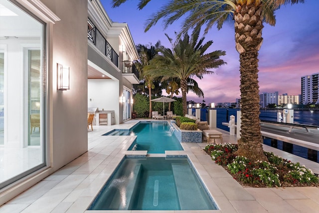 pool at dusk featuring a pool with connected hot tub, a patio area, and a view of city