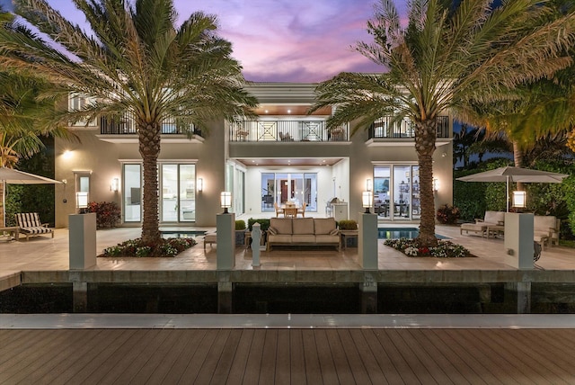 back of house at dusk featuring stucco siding, a patio, an outdoor hangout area, and a balcony