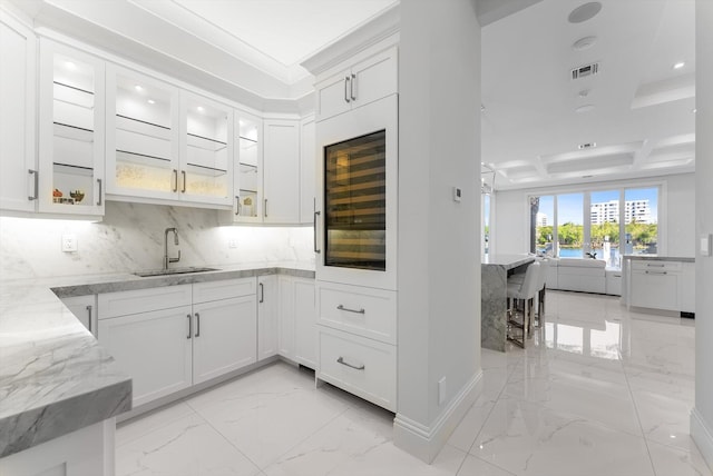 kitchen with light stone countertops, glass insert cabinets, marble finish floor, white cabinetry, and a sink