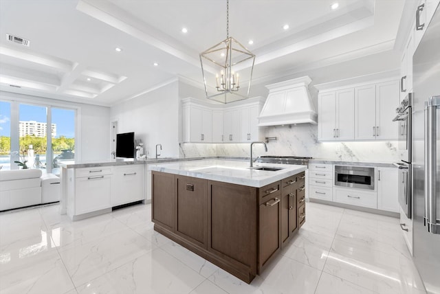 kitchen featuring custom exhaust hood, a peninsula, visible vents, white cabinets, and a center island with sink