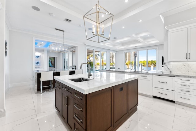 kitchen featuring an island with sink, marble finish floor, decorative light fixtures, white cabinetry, and a sink