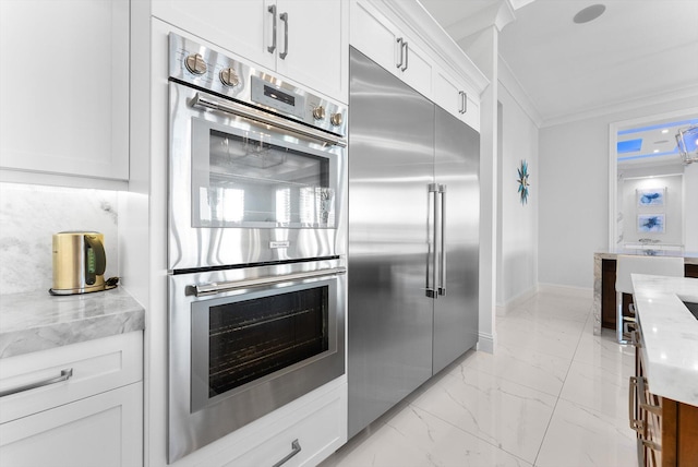 kitchen featuring stainless steel appliances, light stone counters, marble finish floor, ornamental molding, and white cabinets