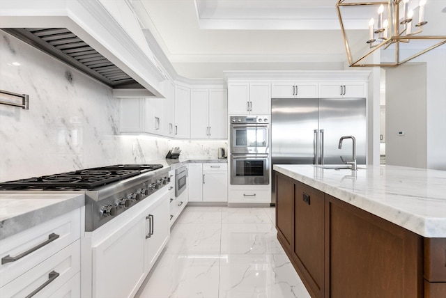 kitchen with white cabinets, custom range hood, marble finish floor, a sink, and built in appliances