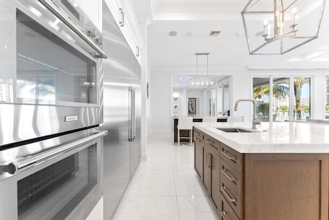 kitchen featuring marble finish floor, pendant lighting, stainless steel appliances, a sink, and light countertops