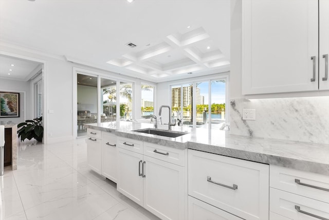 kitchen with coffered ceiling, white cabinetry, light stone countertops, and a sink