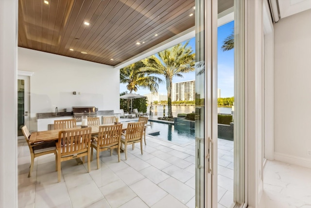 view of patio featuring a water view, a grill, outdoor dining space, exterior kitchen, and a sink