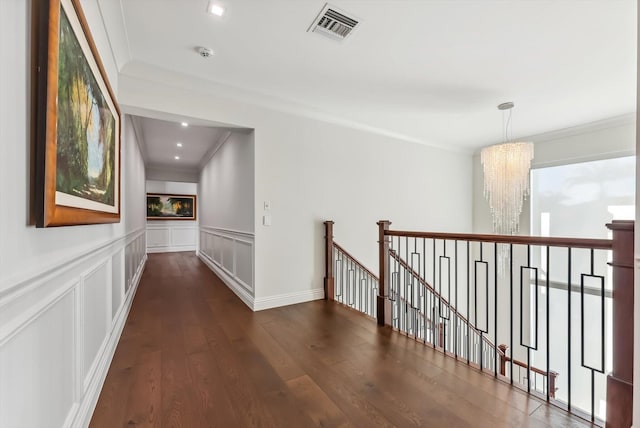 hall featuring a decorative wall, visible vents, an upstairs landing, crown molding, and dark wood-type flooring