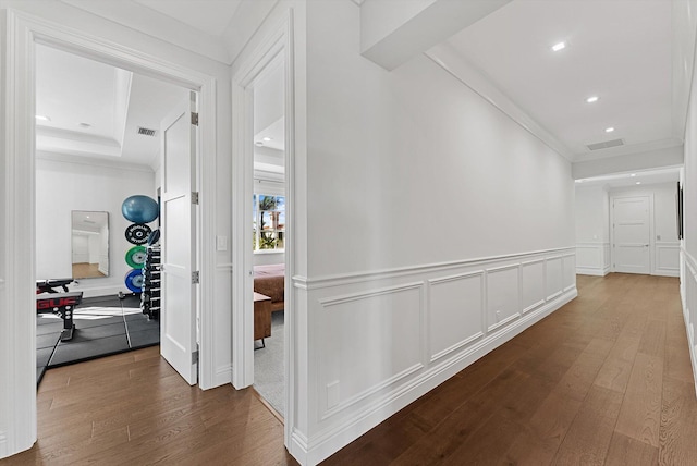 corridor featuring wainscoting, dark wood-type flooring, visible vents, a decorative wall, and crown molding