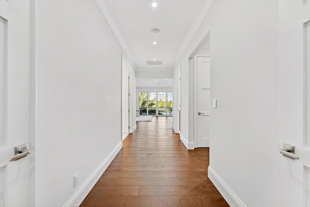 hallway with wood finished floors, baseboards, crown molding, and visible vents