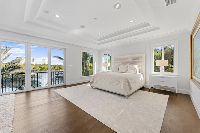 bedroom with a water view, access to outside, visible vents, a raised ceiling, and dark wood finished floors