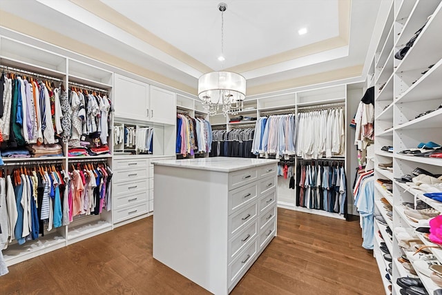 spacious closet featuring dark wood finished floors, an inviting chandelier, and a tray ceiling