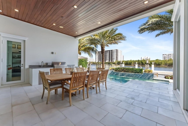 view of patio / terrace featuring outdoor dining space, exterior kitchen, a water view, an outdoor pool, and a sink