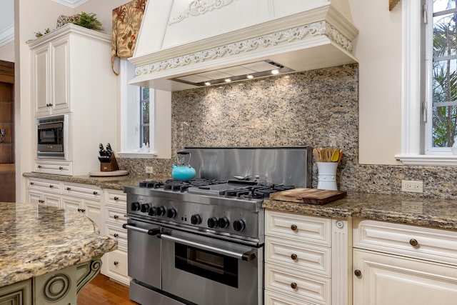 kitchen featuring custom range hood, appliances with stainless steel finishes, dark stone counters, and backsplash