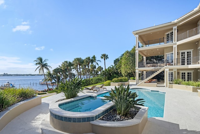 pool with stairs, an in ground hot tub, a patio, and a water view