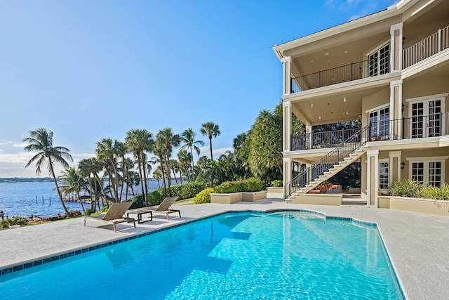 outdoor pool with a patio, french doors, stairway, and a water view