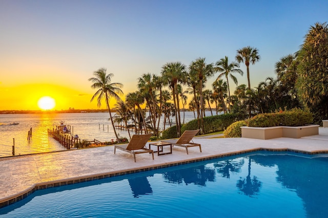 pool at dusk featuring a water view, a patio area, and an outdoor pool